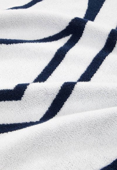 Ύφασμα λευκής υφής με παχιές γεωμετρικές γραμμές σε ναυτικό μπλε που δημιουργούν γωνιώδες μοτίβο, εμφανιζόμενο σε κοντινές πτυχές.