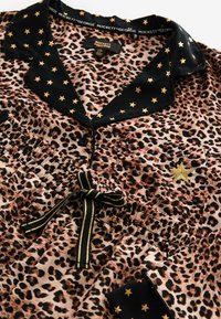 Pajama souprava s leopardím vzorem a černým saténovým límečkem, který má zlaté hvězdy, elastickým pasem a výšivkou zlatých hvězd na kapse.