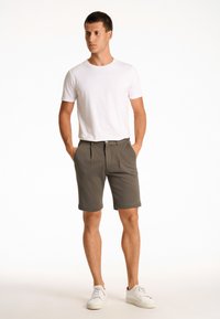 Lichtgrijze shorts met een verzorgd ontwerp, voorzien van voorplooien en zijzakken, gecombineerd met een effen witte T-shirt met ronde hals.