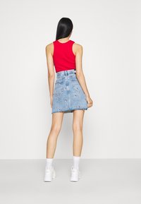 Top rojo sin mangas, falda de mezclilla con diseños bordados y dobladillo deshilachado, combinada con zapatillas blancas y calcetines. Enfoque en atuendos casuales y coloridos.