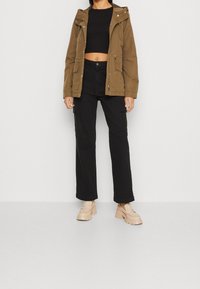 Brun huva jacka med dragkedja, två frontfickor, svarta vida cargobyxor och beige plattformsskor. Platt, slät textur.