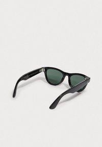 Gafas de sol negras con diseño de ojo de gato, lentes tintados en verde y montura de plástico brillante. Presenta acentos metálicos en las patillas.