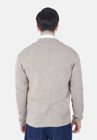 Maglione beige a maglia con maniche lunghe, colletto a scialle e finitura testurizzata, mostrato di spalle sopra pantaloni in denim.