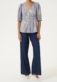 Blusa viola chiaro, con texture, maniche a sbuffo e scollatura a V, dotata di chiusura a bottoni, abbinata a jeans in denim scuri a gamba larga.