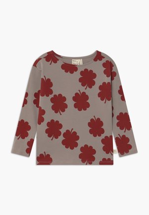 Taupekleurig shirt met lange mouwen en grote rode bloemenklaverpatronen gelijkmatig verdeeld over de voorkant, mouwen en schouders.