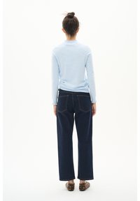 Light blue long-sleeve top with scalloped neckline, paired with dark blue wide-leg jeans. The outfit features a classic denim look.
