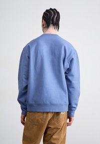 Blå sweatshirt med rund halsudskæring, ribbekanter ved ærmer og kant. Materialet ser blødt ud med en glat tekstur. Bæres med brune kordfløjspants.