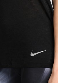 Czarny t-shirt Nike z srebrnym logo po lewej stronie, wykonany z lekkiego materiału o lekko teksturowanej powierzchni.
