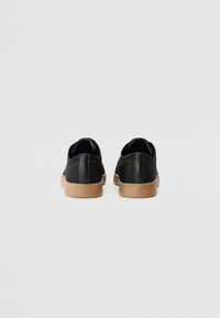 Sneakers neri con tomaia in tessuto a rete, punta tonda, suola in gomma marrone a contrasto e tallone rinforzato. Design semplice, senza motivi visibili.
