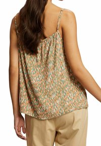 Femme portant un haut loose sans manches avec des bretelles fines et un motif abstrait multicolore, assorti à un pantalon beige.