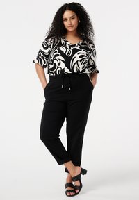 Blouse à motifs en noir et blanc avec un décolleté en V, assortie à un pantalon noir fuselé avec poches et une taille élastique. Sandales à talons noires.