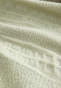 Gros plan sur un tissu doux de couleur crème avec des motifs gaufrés en relief et des rayures.