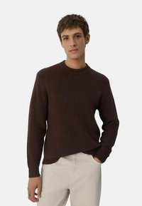 Pruun kudumissé sweater, millel on ribidega ümar kaelus ja pikad varrukad, koos kreemika värvusega pükstega. Tekstuuriga kangas, mis on vabalt keha ümber.