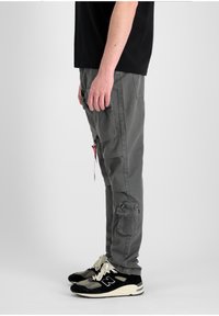 Pantalones cargo grises con múltiples bolsillos, corte recto y una tela texturizada. Combinados con zapatillas negras con suelas y cordones blancos.