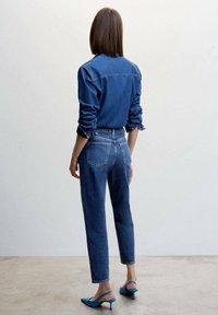 Denimshirt en hoge taille jeans in een donkere wassing, met opgerolde mouwen en achterzakken. Gecombineerd met lichtblauwe slingback hakken.