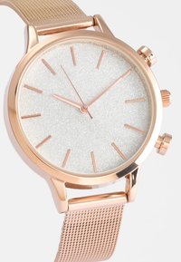 Rose-guld ur med en tekstureret sølvskive, slanke markedere og tre sub-dials. Metalnet-båndet komplementerer det runde kasedesign.