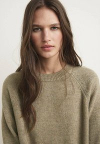 Beige gebreide trui met een ronde hals en ribgebreide accenten. Zachte textuur met een relaxte pasvorm en subtiele kleurvariaties.