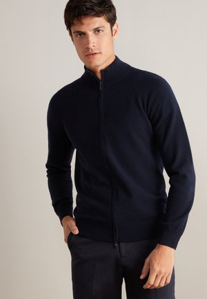 Navy-blaues Zip-Hoodie aus weichem Strickstoff mit hohem Kragen und gerippten Bündchen, das eine taillierte Passform und minimale Nähte aufweist.