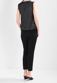 Černý bezramínkový top s texturovanou tkaninou, který má jemný kostkovaný vzor. Spárováno se slim-fit černými kalhotami a vysokými podpatky.