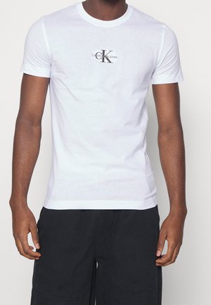 Biała bawełniana koszulka z krótkim rękawem i okrągłym dekoltem. Posiada małe czarne logo "Calvin Klein Jeans" na piersi. Prosty design.