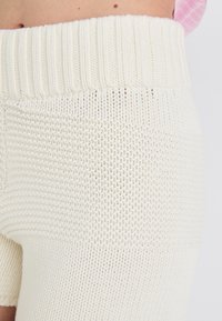 Gebreide crèmekleurige shorts met een brede ribbelband en verschillende textuurpatronen, met een open weef en dichtgebreide segmenten.