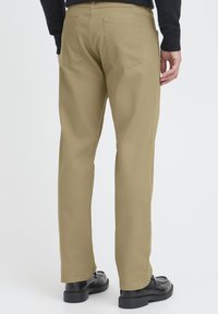 Pantaloni bej din bumbac, croială dreptă, cu două buzunare în spate și finisaj texturat, asortați cu pantofi negri lucioși.