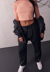 Light pink cropped long-sleeve top with a logo, black quilted jacket, black pants with gold accents, and white sneakers.