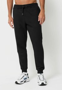 Melni sporta bikses ar elastīgu jostu un auklu, ar sašaurinātu kāju dizainu. Tekstūrēta kokvilnas auduma, apvienotas ar baltām sporta kurpēm.