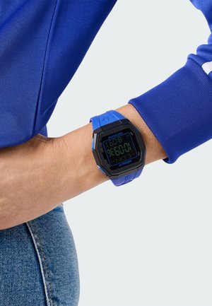 Montre numérique avec un boîtier octogonal noir et bleu, un bracelet en silicone bleu et un écran numérique affichant l'heure et des fonctionnalités de chronomètre.