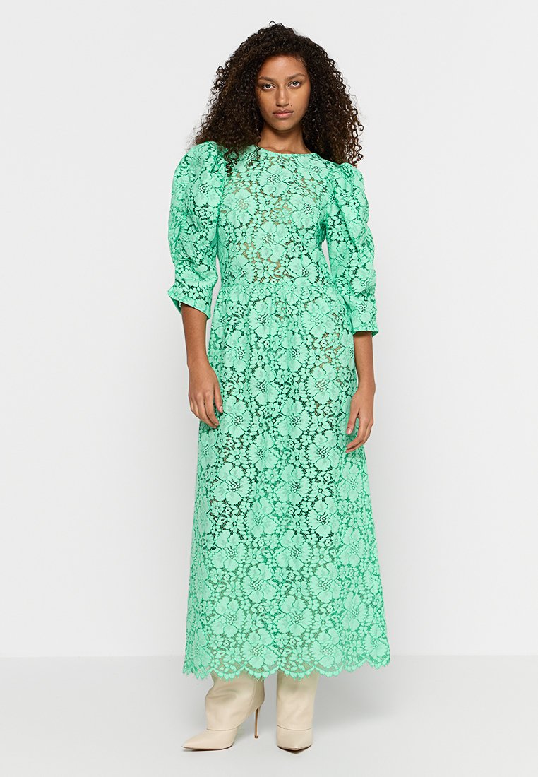 Mintgrünes Spitzenkleid mit Puffärmeln, bodenlang, mit scallopfähniger Saum und kompliziertem Blumenmuster, kombiniert mit beigen Absatzstiefeln.