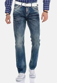 Blauwe spijkerbroek met een rechte pasvorm, lichte vervaging, contrasterende stiksels en voorzakken. Gecombineerd met witte sneakers en een riem.