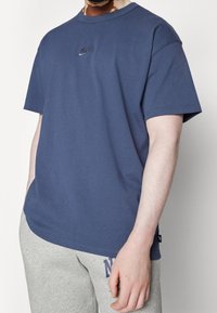 Mörkblå bomull t-shirt med korta ärmar, rund halsringning och en liten broderad Nike-logotyp på bröstet. Slät textur, avslappnad passform.