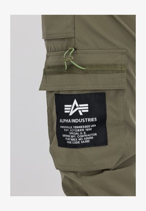 Olivenfarvede stof cargo bukser med et patch med sort baggrund og hvid tekst, justerbar snor og flere lommer.