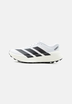 Chaussure de trail running blanche avec des bandes noires Adidas, semelle texturée et marquage "TERREX" sur le talon, affichée de profil sur fond blanc.