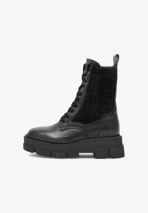 Čierne členkové topánky s hladkým koženým špičkou a hrubou gumovou podrážkou. Zvršok obsahuje huňaté čierne textilné panely a pevným šnúrky.