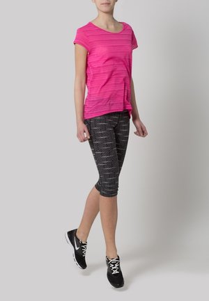 Camisa de manga corta a rayas rosas combinada con leggins capri negros con patrones de puntos blancos y zapatillas deportivas negras con cordones blancos.