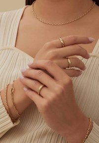 Goldschmuckset, bestehend aus einer zarten Kettenhalskette, drei Ringen mit unterschiedlichen Designs und einem Armband, das alles auf akzentuierten Hauttönen präsentiert wird.