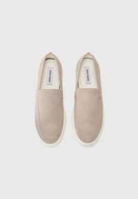 Beige semskede slippers med en glat tekstur, som har en hvid gummisål og syet detaljer langs kanterne.