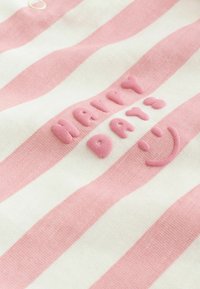 Roza i bijela tkanina s vodoravnim prugama, s ispisanim uzdignutim ružičastim tekstom "SRETAN DAN :)" i nacrtanim smiješkom.