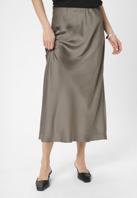 Mellemlang nederdel i glat, olivengrøn satin med elastisk talje. Har en subtil tekstur og falder smukt. Bæres med flade, sorte sko.