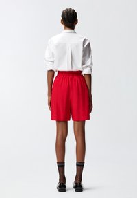 Pantaloni rossi con cintura elastica, abbinati a una maglietta bianca. Scarpe nere e calze a rete completano il look.