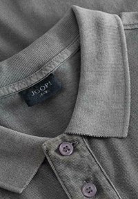 Polo gris avec un tissage texturé, col côtelé et deux boutons violets. Une étiquette noire avec "JOOP!" est visible au col.