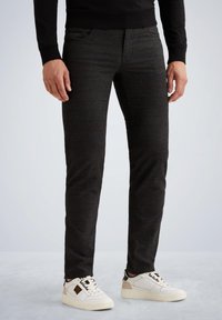 Zwarte denim jeans met een gestructureerde afwerking, slim fit, vijf-pocket ontwerp, gecombineerd met witte sneakers met zwarte en beige accenten.