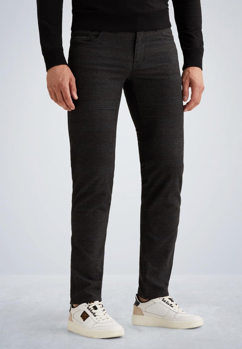 Zwarte denim jeans met een gestructureerde afwerking, slim fit, vijf-pocket ontwerp, gecombineerd met witte sneakers met zwarte en beige accenten.