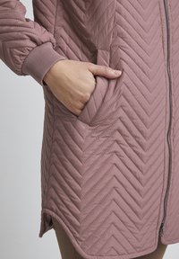 Prošívaná růžová bunda s vzorem chevron, s uzavíráním na zip, manžetami s žebrovaným vzorem a bočními kapsami pro zvýšení funkčnosti. Hladký, lehký materiál.
