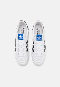 Sneakers in pelle bianca con tre strisce nere, una targhetta logo blu, punta rotonda e cuciture testurizzate sulla parte anteriore.