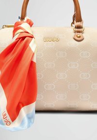 Borsa in pelle beige con motivo embossato, logo dorato e manici marroni. Una sciarpa colorata attaccata presenta un design in rosso, bianco e blu.