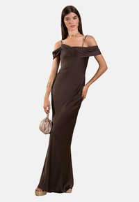 Braunes schulterfreies Kleid aus glattem Stoff, mit einem drapierten Ausschnitt und einer taillierten Silhouette. Kombiniert mit einer hellfarbigen Tasche.