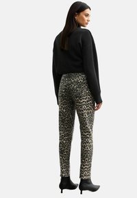 Leopardmönstrade byxor med en figurnära design, i beige och svart färg, av denim-material, i kombination med en svart tröja och ankelstövlar.