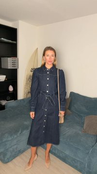 Denim skjortekjole, mørk blå, knappeåpning, lange puffermede ermer, beltedetalj ved midjen, stylet med nude hæler og en liten håndveske.